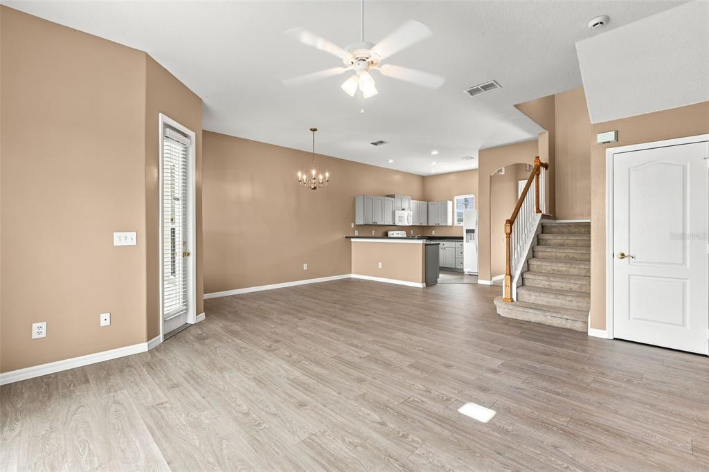 An open-concept living and dining area features light wood-look flooring, beige walls, and a staircase — 516 BRUNELLO DRIVE, DAVENPORT, FL