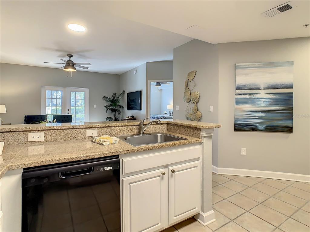A kitchen sink and dishwasher are set into a granite countertop in this open-concept room — 7503 ATLANTIS WAY UNIT J102, KISSIMMEE, FL