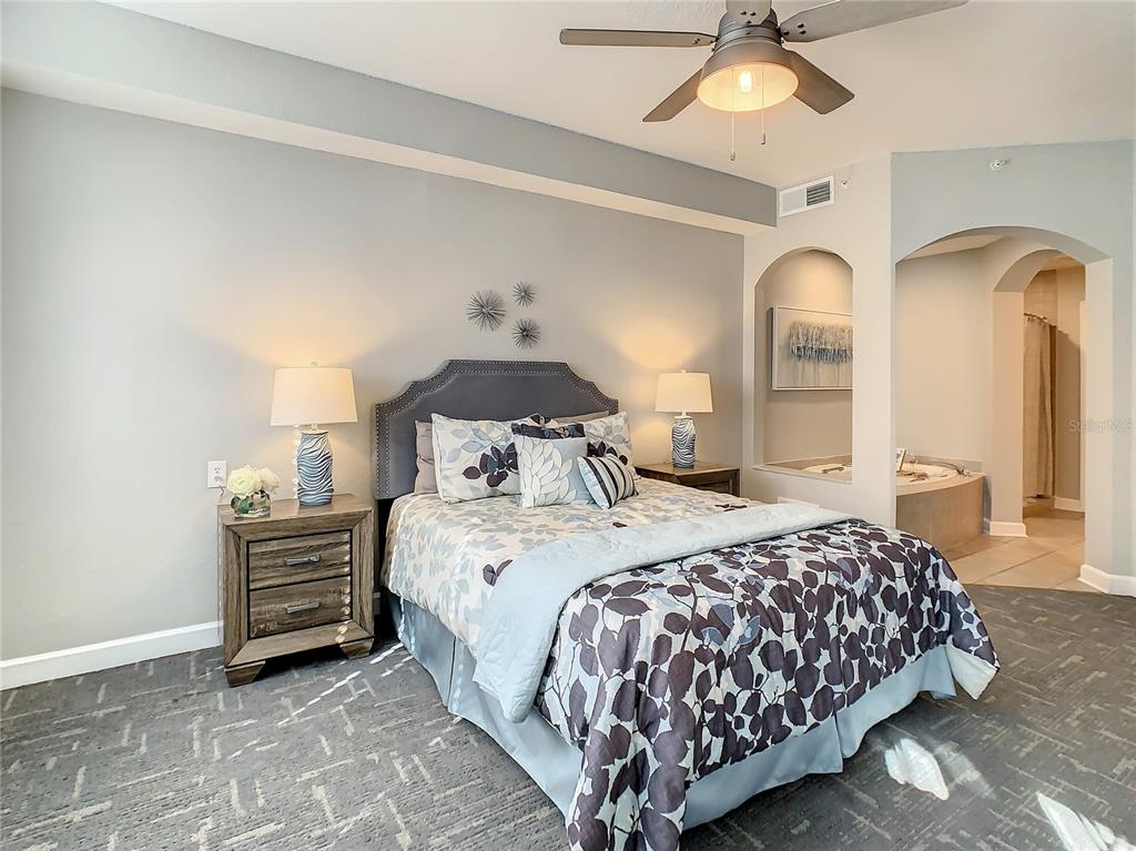 A bedroom features a bed with patterned bedding, two nightstands, and an adjacent bathroom alcove — 7503 ATLANTIS WAY UNIT J102, KISSIMMEE, FL