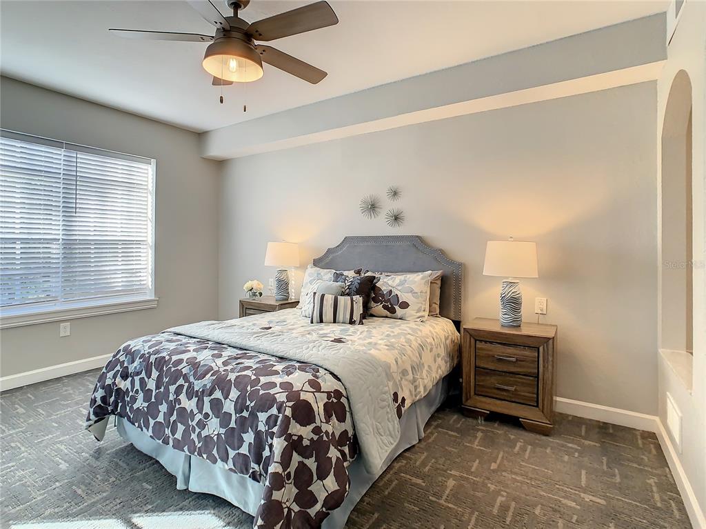 A bedroom features a bed with patterned bedding, two nightstands with lamps, and a ceiling fan — 7503 ATLANTIS WAY UNIT J102, KISSIMMEE, FL
