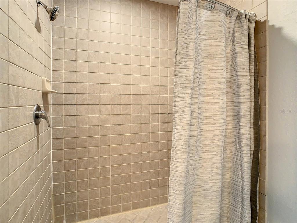 A tiled shower stall features a showerhead, a faucet, and a hanging shower curtain — 7503 ATLANTIS WAY UNIT J102, KISSIMMEE, FL
