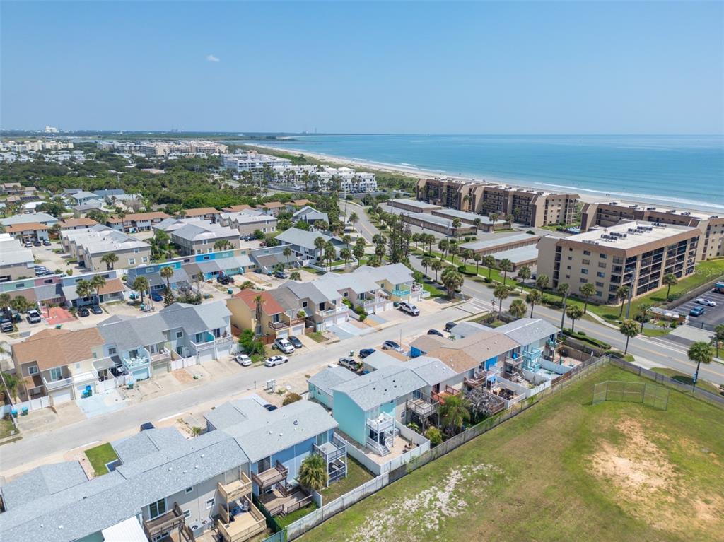 An aerial view shows a coastal neighborhood with multi-story houses, palm trees, and the ocean — 241 CHERIE DOWN LANE, CAPE CANAVERAL, FL