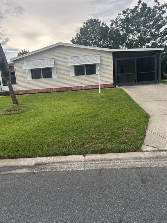 A single-story house with light siding, a concrete driveway, and a screened-in porch — 1550 HILLCREST DRIVE, THE VILLAGES, FL