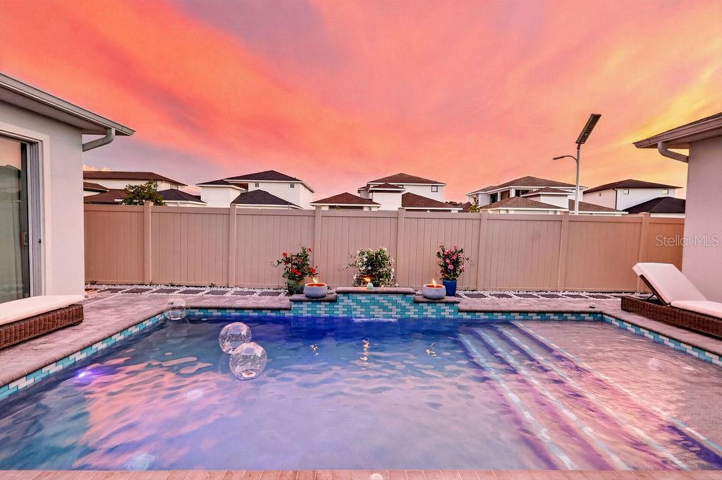 A swimming pool with floating balls sits in a backyard at sunset with a fence — 10470 PURPLE THISTLE WAY, SAN ANTONIO, FL