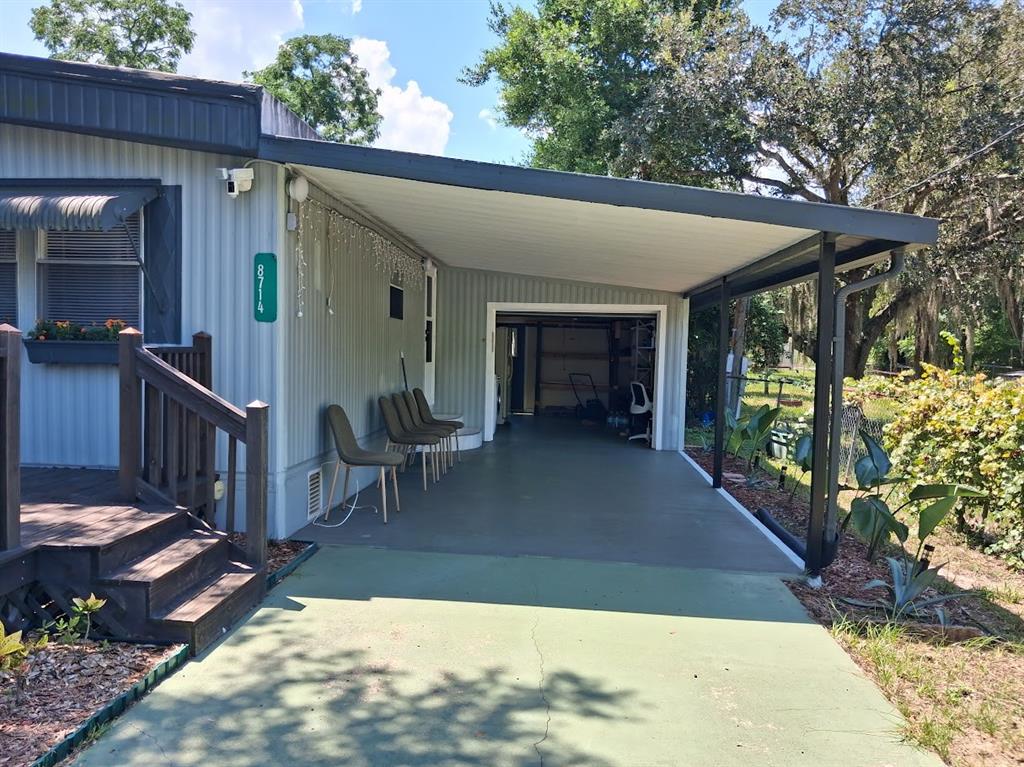 A mobile home exterior features a covered carport, a wooden deck, and a green driveway — 8714 ALLAMANDA STREET, HUDSON, FL