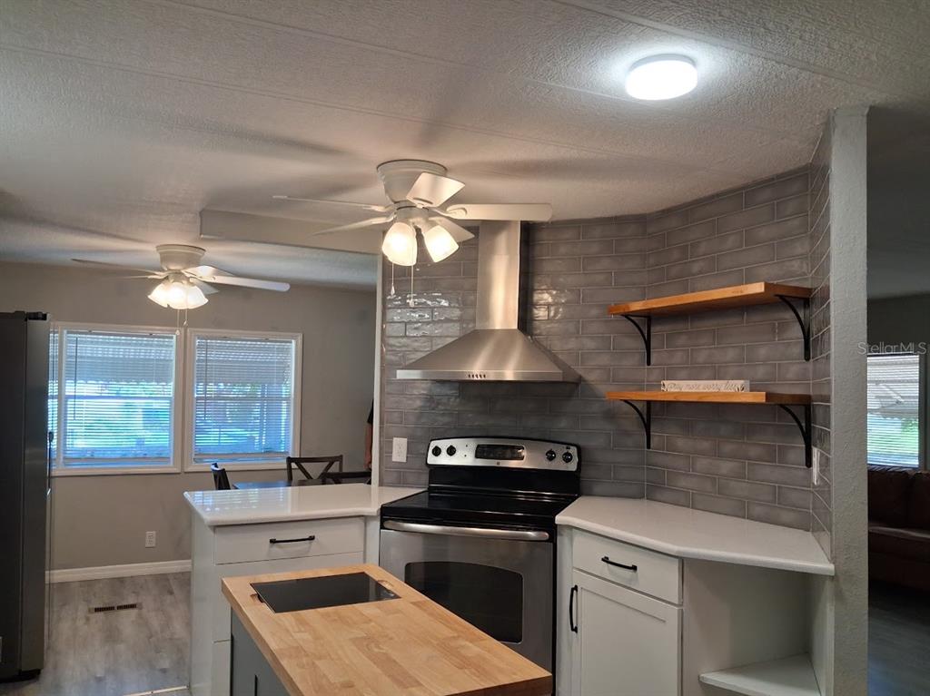 A kitchen features white cabinets, a butcher block island, stainless steel appliances, and gray tile — 8714 ALLAMANDA STREET, HUDSON, FL