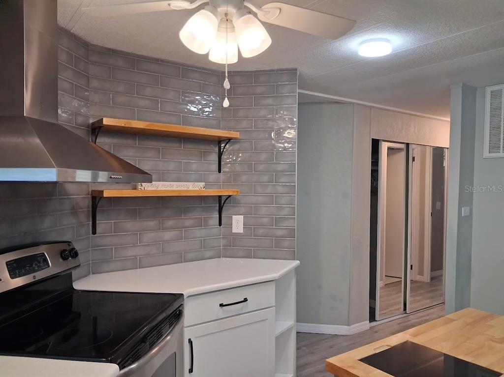A kitchen features gray subway tile backsplash, open wood shelving, white cabinets, and stainless appliances — 8714 ALLAMANDA STREET, HUDSON, FL