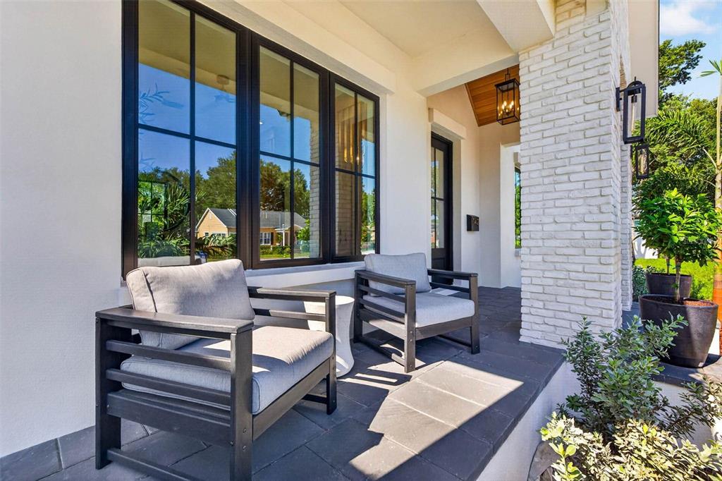 A covered front porch features dark tile flooring, two modern chairs, and white brick accents — 142 22ND AVENUE N, ST PETERSBURG, FL