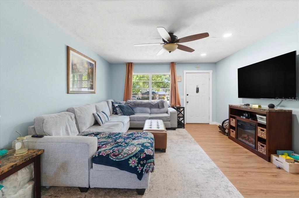 A living room features a light gray sectional sofa, a television, and wood-look flooring — 215 CARLA ANN COURT, AUBURNDALE, FL