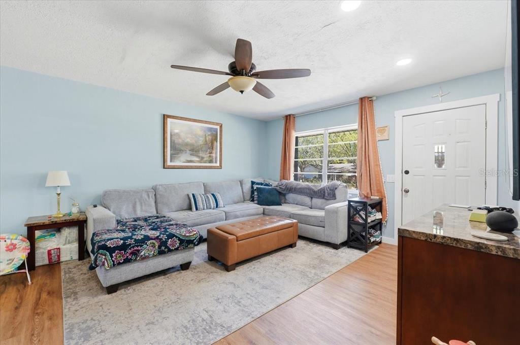 A living room features a light blue wall, a gray sectional sofa, and wood-look flooring — 215 CARLA ANN COURT, AUBURNDALE, FL