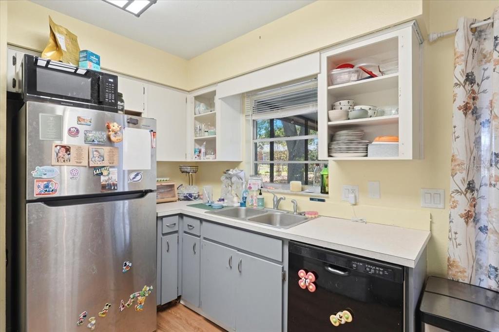 A kitchen features a stainless steel refrigerator, gray cabinets, a double sink, and open shelving — 215 CARLA ANN COURT, AUBURNDALE, FL