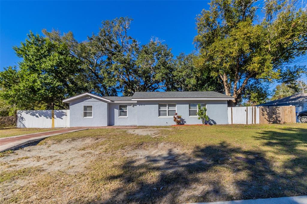 A single-story gray house with a shingled roof sits behind a large, patchy lawn — 4933 BALBOA DRIVE, ORLANDO, FL