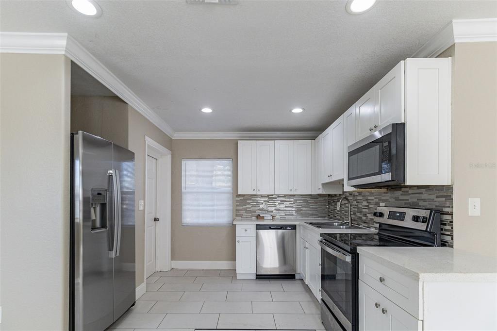 A kitchen with white cabinets, stainless steel appliances, and light-colored tile flooring — 4933 BALBOA DRIVE, ORLANDO, FL