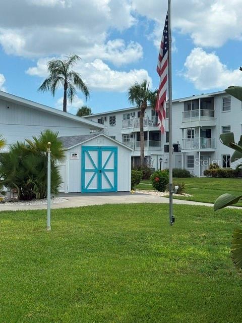 A small shed with bright blue doors stands on a lawn near a multi-story building — 2223 SUNSET DRIVE UNIT E24, BRADENTON, FL