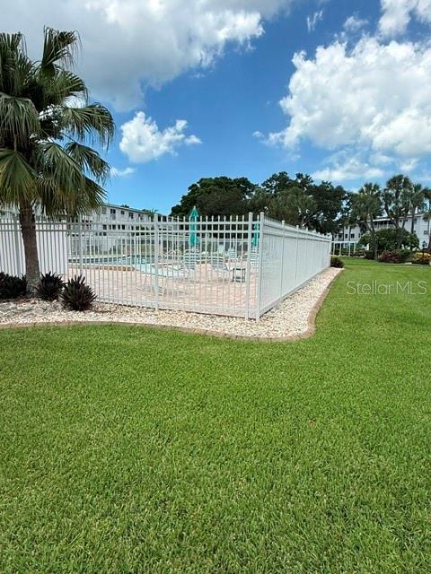 A white metal fence encloses a swimming pool area surrounded by grass and palm trees — 2223 SUNSET DRIVE UNIT E24, BRADENTON, FL