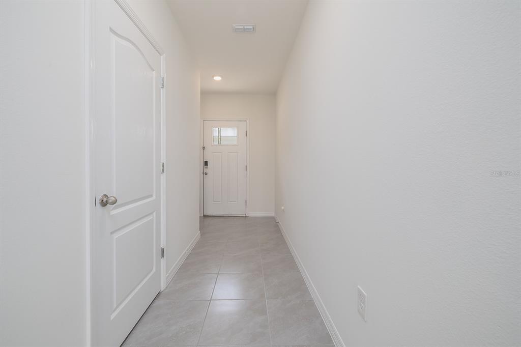 A hallway with light gray tile flooring, white walls, and a white front door — 58 BELLA OAKS DRIVE, PORT ORANGE, FL