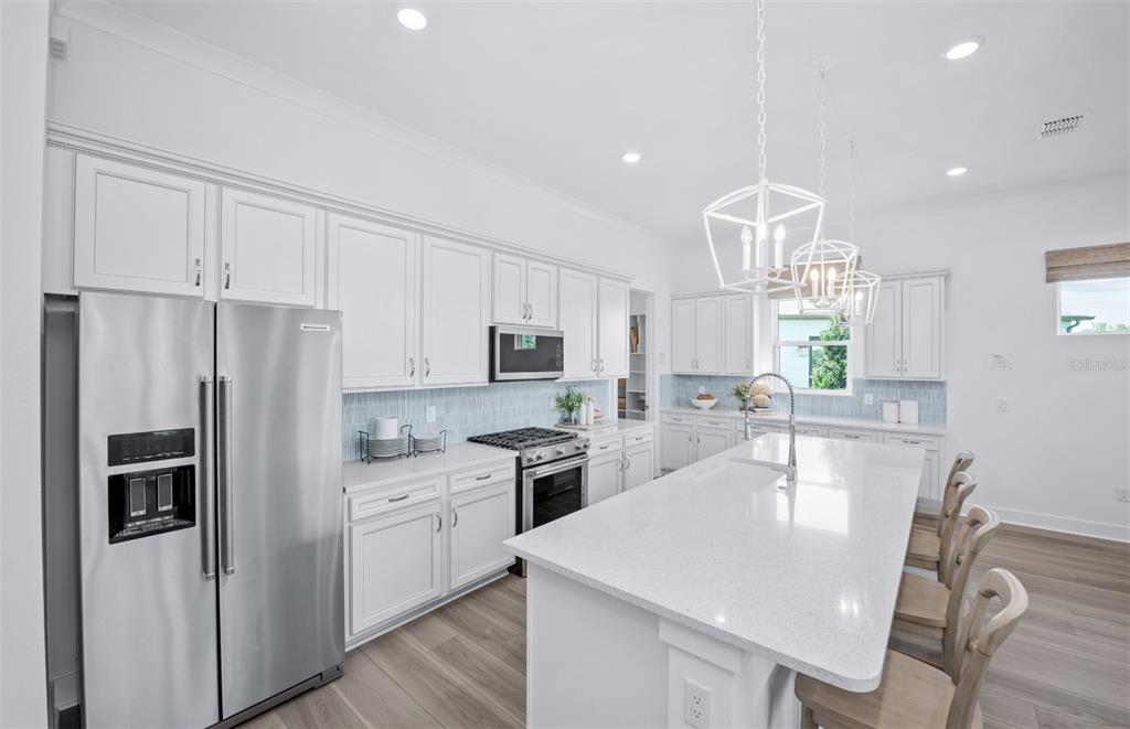 A bright kitchen features white cabinets, stainless steel appliances, a large island, and light flooring — 11316 CLAY AVENUE, PARRISH, FL
