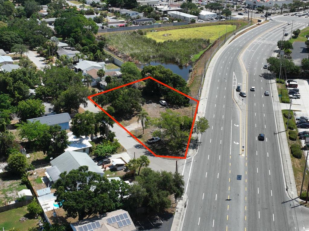 An aerial view shows a vacant, tree-covered lot outlined in red next to a highway — ALBERT PLACE, SARASOTA, FL