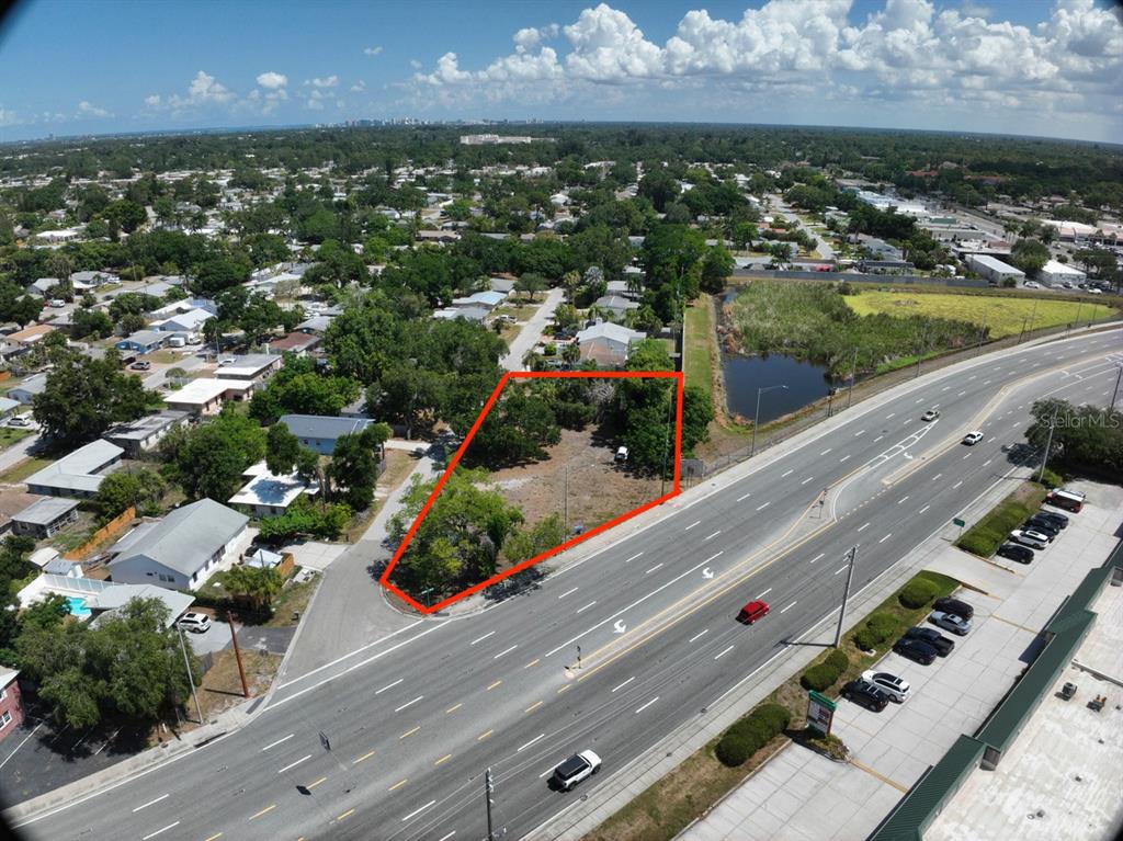 An aerial view shows a vacant, tree-covered lot outlined in red next to a highway — ALBERT PLACE, SARASOTA, FL