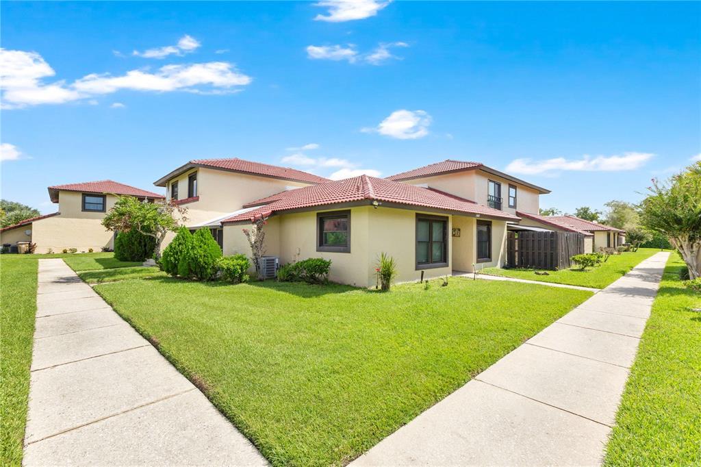 A two-story townhouse with a tan exterior, red tile roof, and surrounding green lawn — 545 HUNTER CIRCLE, KISSIMMEE, FL