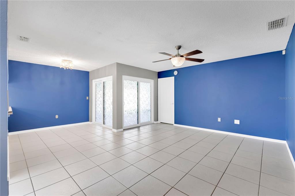 An empty room features blue walls, white tile flooring, a ceiling fan, and sliding glass doors — 545 HUNTER CIRCLE, KISSIMMEE, FL