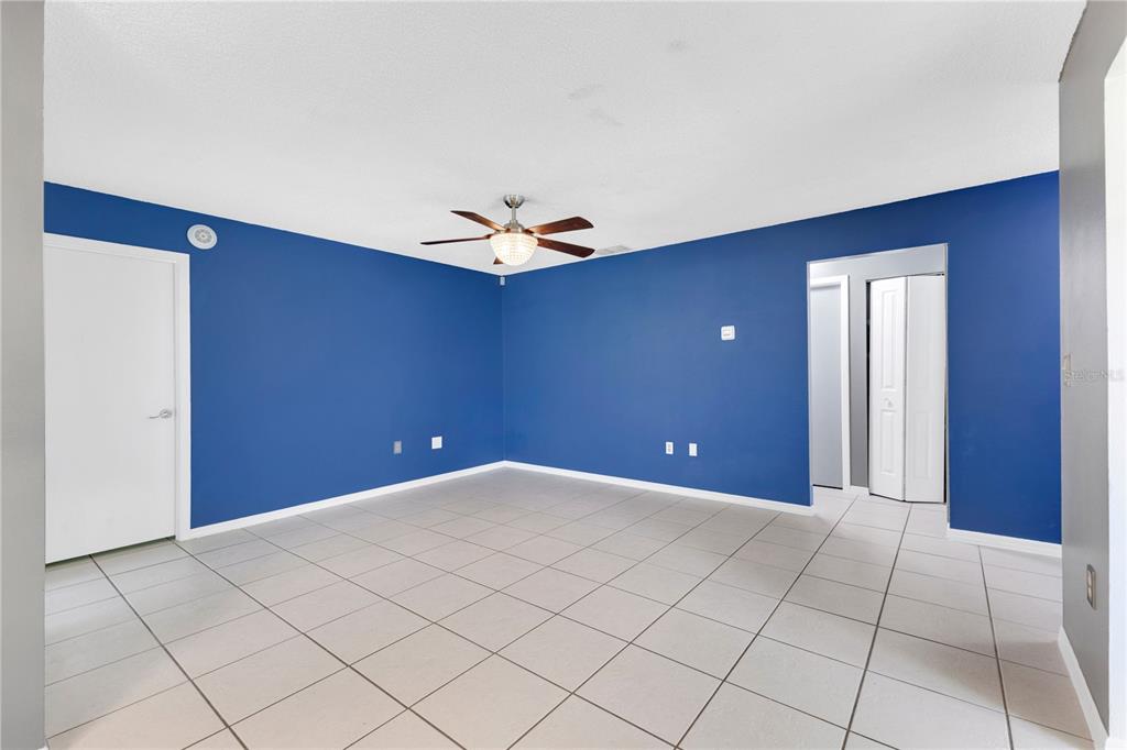 An empty room with blue walls, a ceiling fan, and light-colored tiled flooring — 545 HUNTER CIRCLE, KISSIMMEE, FL