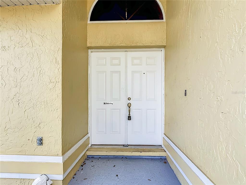 A white double front door with a transom window sits in a yellow stucco entryway — 2108 JONATHAN LANE, WINTER HAVEN, FL