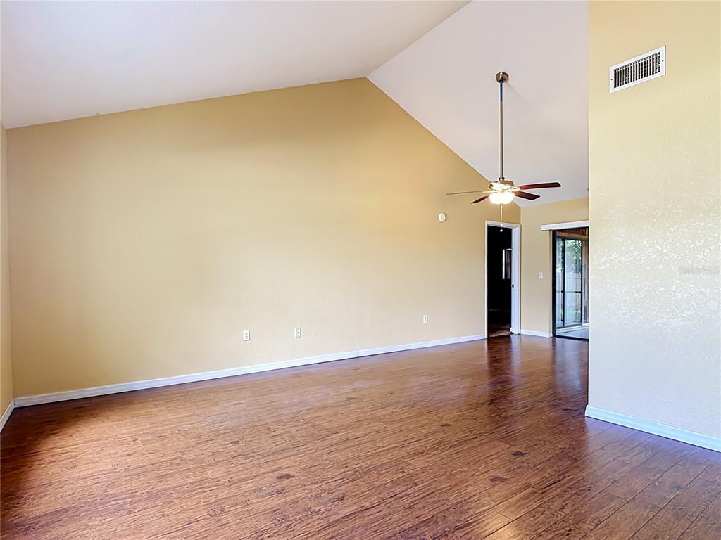 An empty living room features vaulted ceilings, wood-look flooring, and a ceiling fan — 2108 JONATHAN LANE, WINTER HAVEN, FL