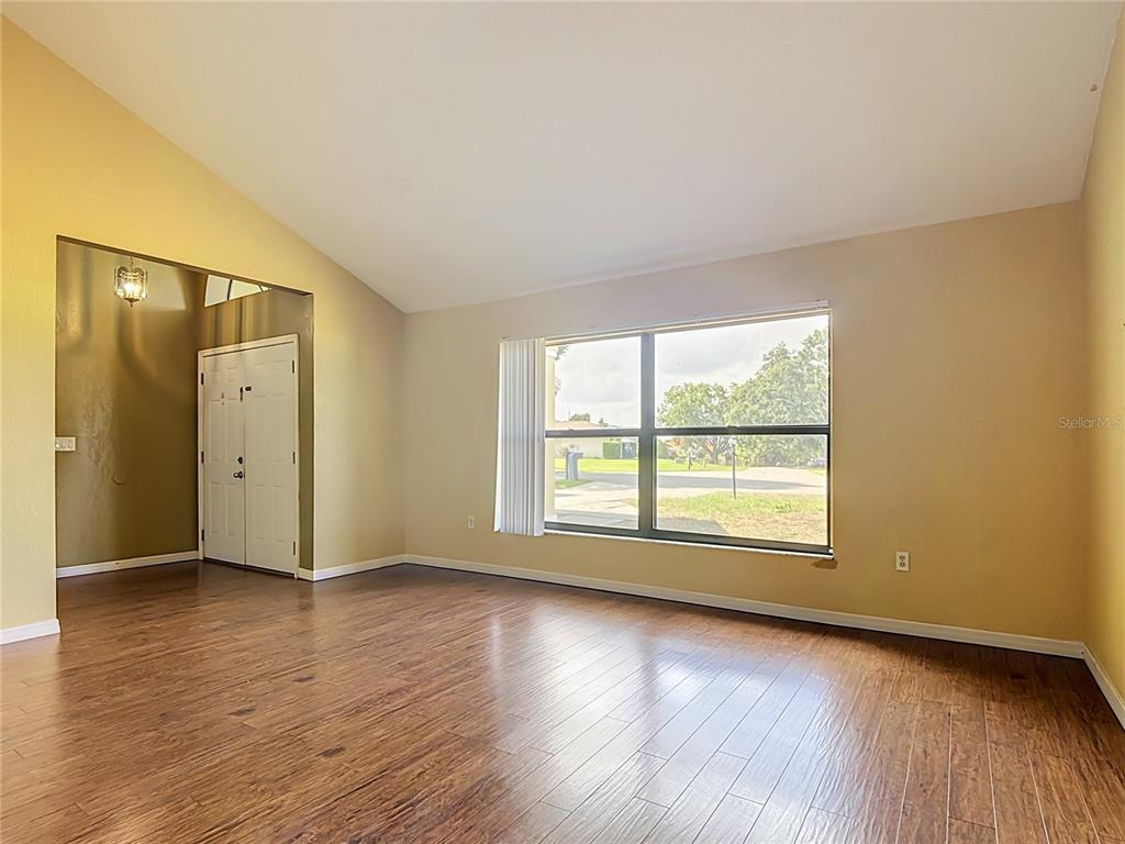 An empty room features wood-look flooring, a vaulted ceiling, and a large window — 2108 JONATHAN LANE, WINTER HAVEN, FL