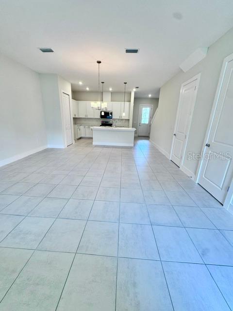 An open-concept kitchen with white cabinetry and a central island overlooks a tiled living area — 1519 HERITAGE PLACE, OVIEDO, FL