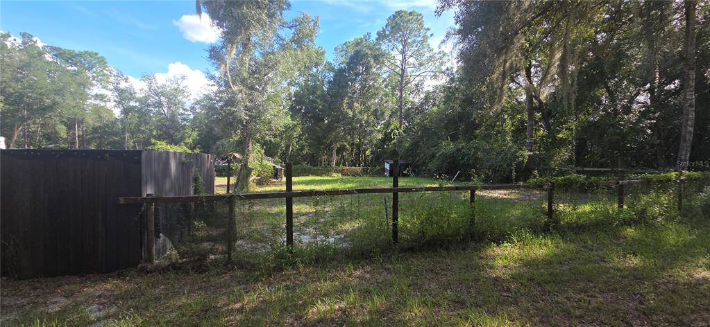 A fenced-in backyard features a wooden structure, mature trees, and a grassy lawn — 407 RAULERSON ROAD, SEVILLE, FL