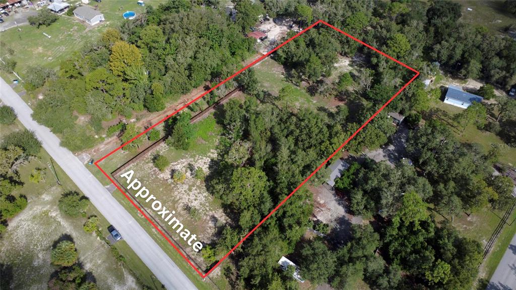 A grassy, sunlit lot is surrounded by mature trees under a blue sky with clouds — 14535 LITTLE RANCH ROAD, SPRING HILL, FL