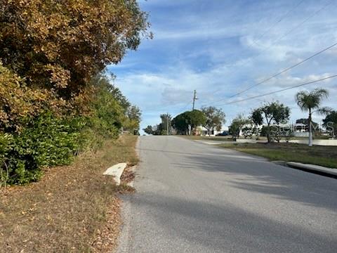 A paved road leads uphill past trees and a residential area under a blue sky — SUNSET TRAIL, BABSON PARK, FL
