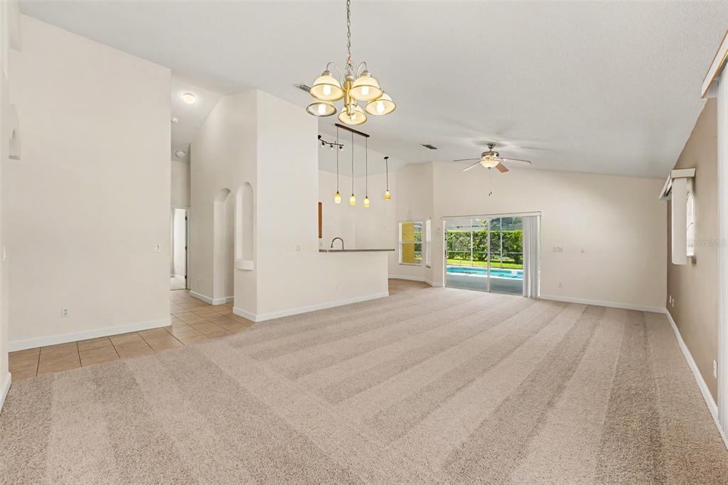 A spacious living room with beige carpet, a breakfast bar, and sliding glass doors to a pool — 131 OLD BRIDGE CIRCLE, DAVENPORT, FL
