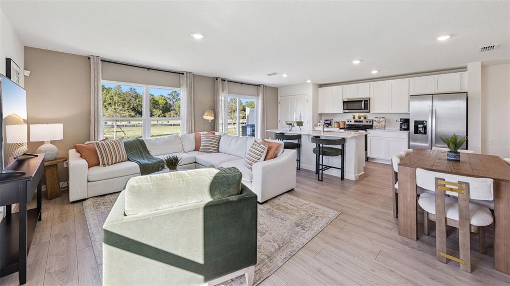 An open-concept living room and kitchen feature white cabinets, stainless appliances, and light wood flooring — 479 REMICK STREET, OSTEEN, FL