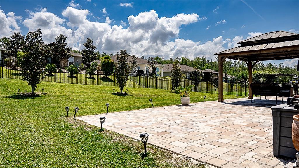 The backyard features a paved patio with a gazebo, lawn, and surrounding privacy fences — 5526 LIMESTONE STREET, MOUNT DORA, FL