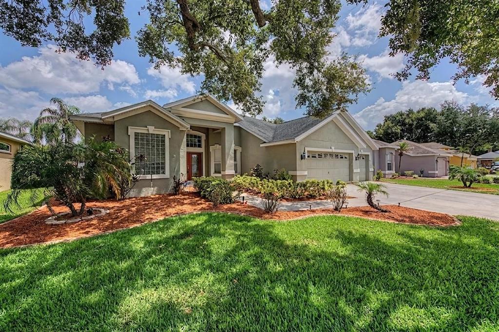A single-story suburban house with a tan exterior, a three-car garage, and landscaped front yard — 4332 SWIFT CIRCLE, VALRICO, FL