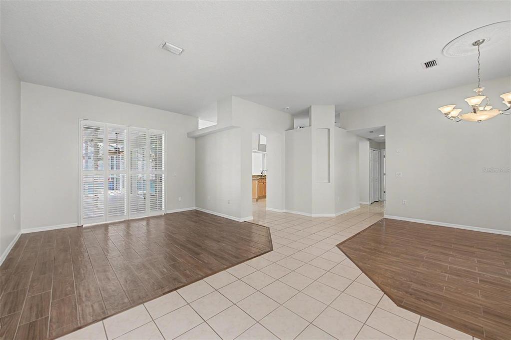 An open-concept living and dining area features wood-look tile flooring, white walls, and sliding doors — 4332 SWIFT CIRCLE, VALRICO, FL