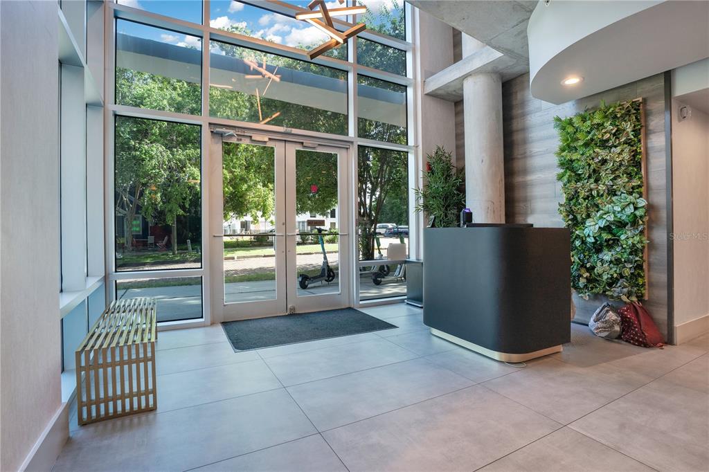 A modern building lobby features floor-to-ceiling windows, a reception desk, and a vertical garden wall — 525 E JACKSON STREET UNIT 403, ORLANDO, FL