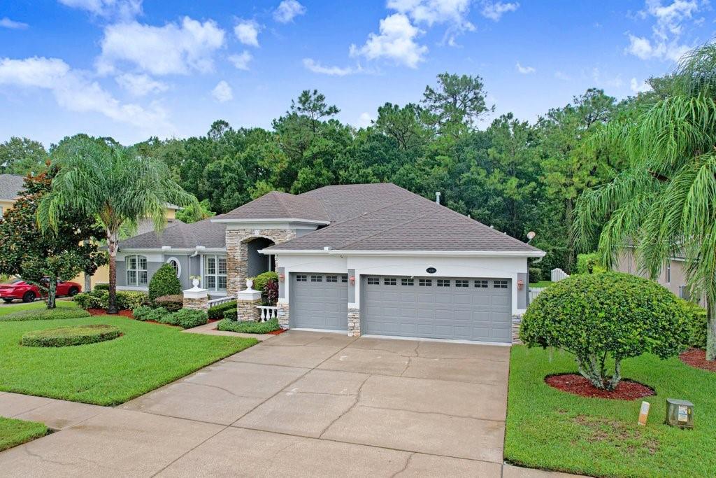A single-story house with a gray three-car garage, stone accents, and a manicured green lawn — 16116 IVY LAKE DRIVE, ODESSA, FL