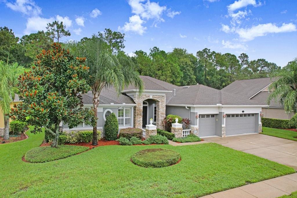 A single-story house with a stone-accented entryway, gray exterior, and a three-car garage — 16116 IVY LAKE DRIVE, ODESSA, FL