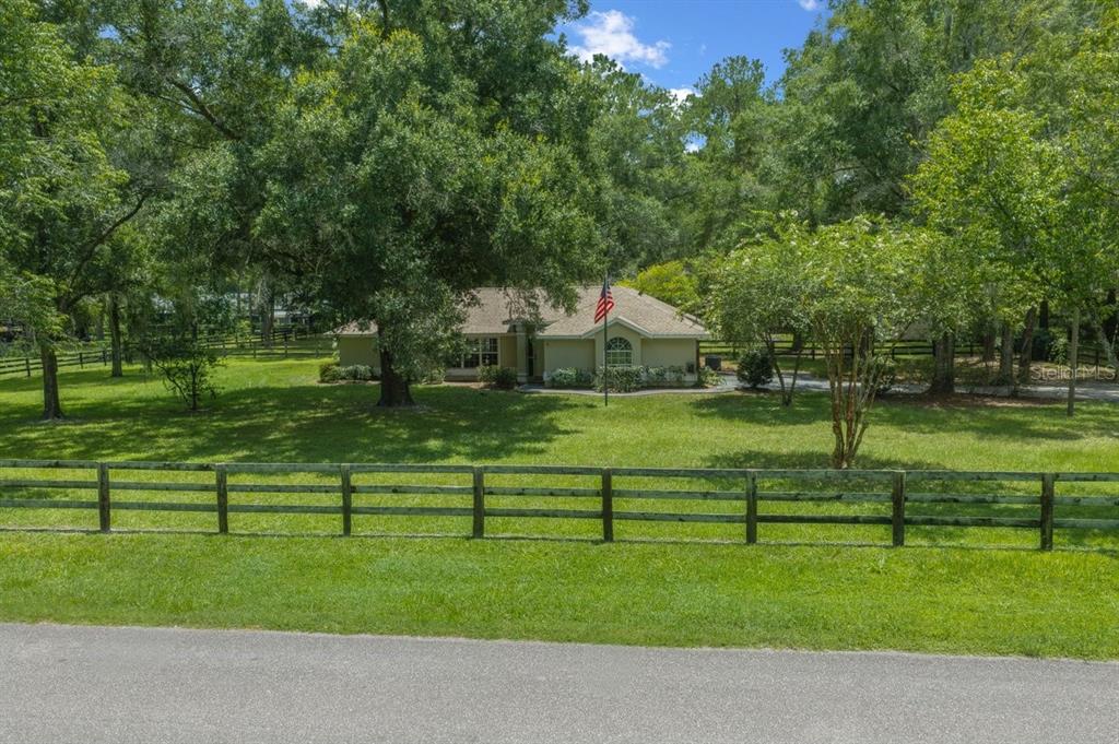 A single-story house sits behind a wooden fence on a large, tree-filled grassy lot — 4 HIALEAH DRIVE, OCALA, FL