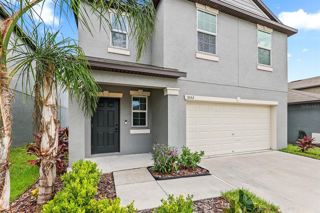 A two-story gray house features a front door, a garage, and a small landscaped garden — 5552 BLUE AZURE DRIVE, WIMAUMA, FL