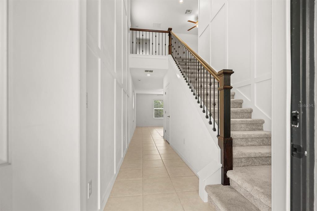 A bright entryway features a tiled floor, white paneled walls, and a carpeted staircase — 5552 BLUE AZURE DRIVE, WIMAUMA, FL