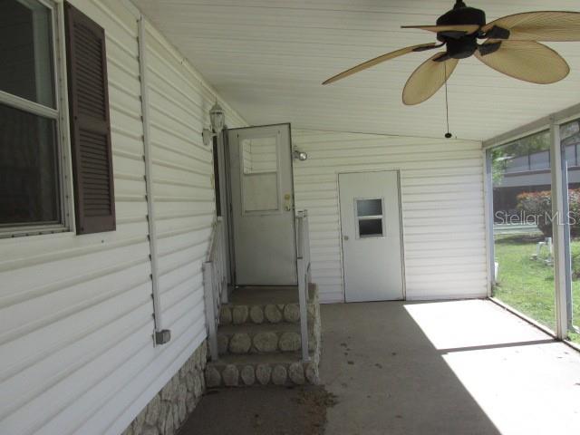 A covered porch with a ceiling fan, concrete floor, and two white exterior doors — 2537 LONGPINE LANE, ST CLOUD, FL