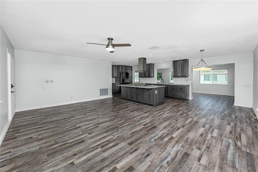 An open-concept kitchen with dark cabinetry and a large island overlooks a spacious living area — 3455 100TH AVENUE N, PINELLAS PARK, FL