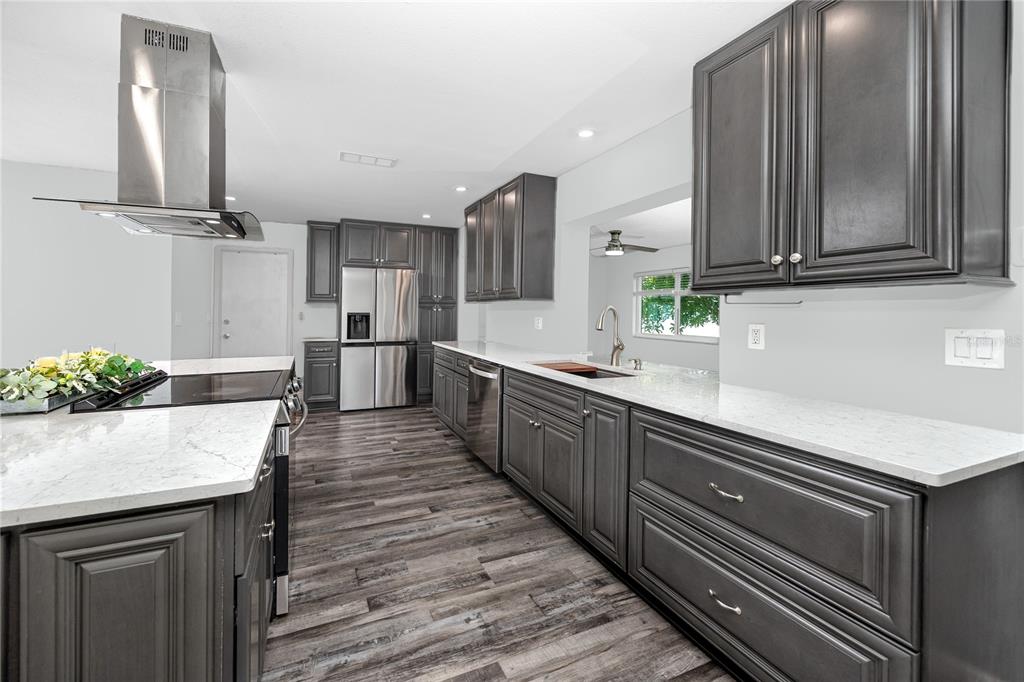 A kitchen features dark gray cabinetry, white countertops, stainless steel appliances, and wood-look flooring — 3455 100TH AVENUE N, PINELLAS PARK, FL