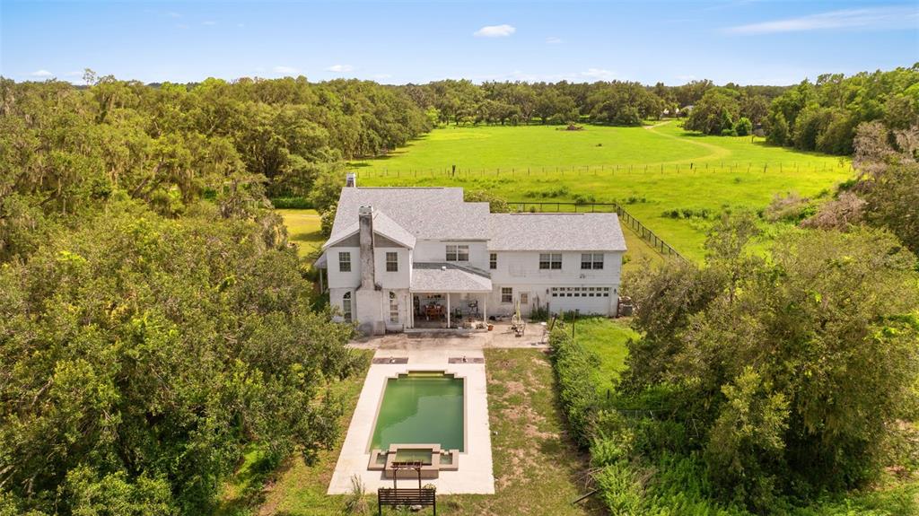 An aerial view of a two-story house with a swimming pool and surrounding green fields — 13621 MCINTOSH ROAD, THONOTOSASSA, FL