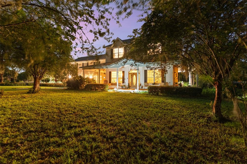 A two-story house with a covered front porch sits on a grassy lawn at dusk — 13621 MCINTOSH ROAD, THONOTOSASSA, FL