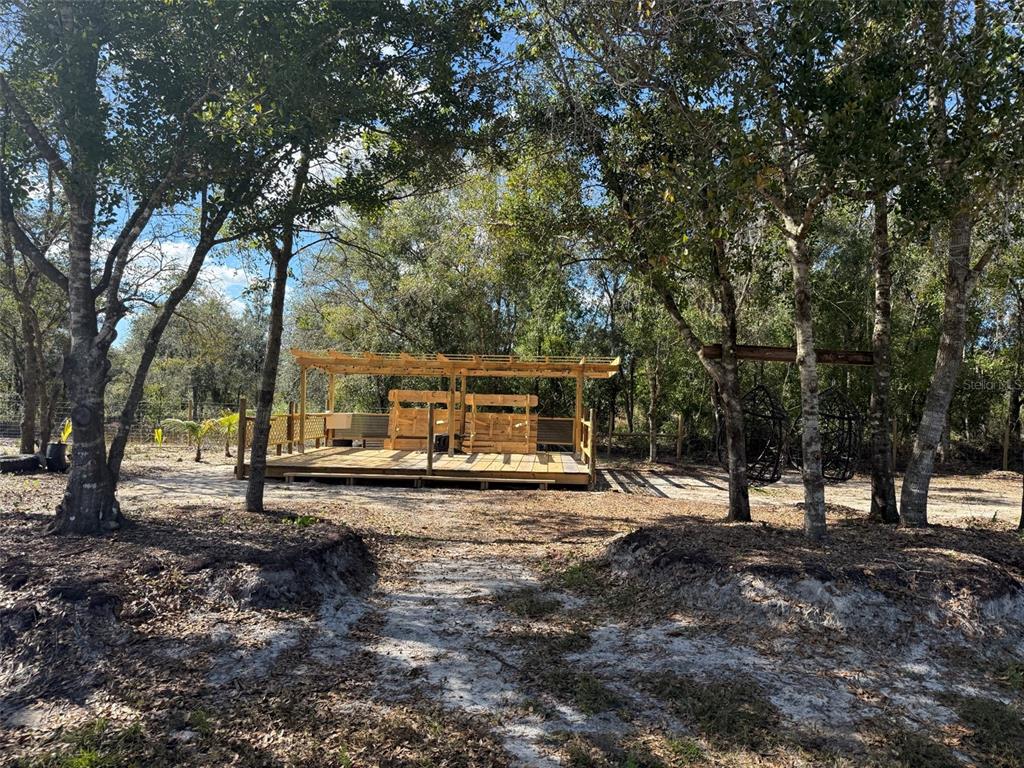 A wooden pergola structure with a deck sits in a wooded area with hanging chairs — 17618 NW 286TH STREET, OKEECHOBEE, FL